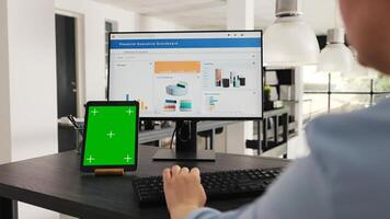 Employee checks tablet with greenscreen while she works on business operations at desk, looking at modern gadget presenting isolated copyspace display. Woman looks at mockup layout. Handheld shot. photo