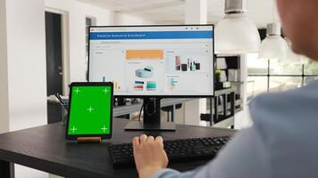 empleado cheques tableta con pantalla verde mientras ella trabajos en negocio operaciones a escritorio, mirando a moderno artilugio presentación aislado copyspace mostrar. mujer mira a Bosquejo disposición. Mano disparo. foto