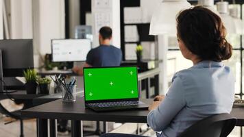 Employee checks greenscreen on laptop, looking at isolated copyspace mockup screen in coworking space. Young woman reviewing pc display layout with blank chromakey template. Handheld shot. photo