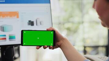 Specialist looks at greenscreen display on mobile phone, holding gadget with copyspace isolated software at workstation. Employee working with blank mockup layout in business office. Close up. photo