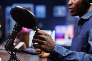 Black man uses professional mic to record a podcast in home studio. Close up shows african american person touching modern condenser microphone and speaking into it while doing radio show. photo