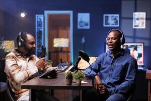 Program host and guest conversing in an elaborate home studio with neon lighting. African american influencers use professional equipment to broadcast a discussion on online podcast episode. photo