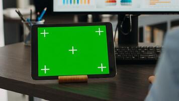 Startup specialist looks at digital tablet with greenscreen, using gadget with blank chromakey template. Person working at desk with isolated mockup copyspace, checking marketing data. Close up. photo