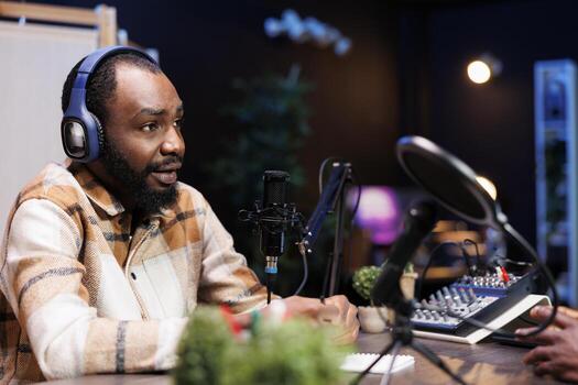 Man talk show host using audio equipment and having a friendly interview with an upcoming artist at home studio. African american content creator with headphones and microphone is creating a podcast. photo