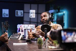 Talking with a guest, the show host uses a camera mounted on a tripod stabilizer to record a video for social media platforms. Male influencer using professional equipment to record a vlog at home. photo