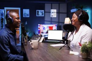 Cheerful couple are conversing while the laptop displays a blank copyspace mockup template. A portable computer displays an isolated white screen template that advertises an online streaming platform. photo