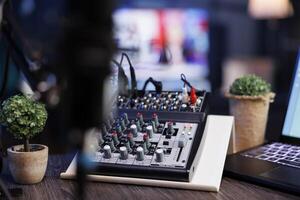 Selective focus on laptop keyboard and audio mixer knobs on a podcasting desk in the home studio. Detailed view of buttons on professional sound equipment used for live internet broadcasts. photo