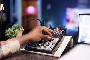 Detailed view of black person adjusting sound mixer to achieve high-quality recording during the podcast episode. African american individual turning an audio equipment knob while hosting a talk show. photo