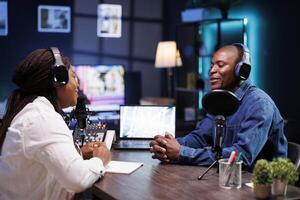 Female interviewer having live discussion with black man, recording a radio show. African american couple using audio equipment in home studio, talking and making a podcast episode. photo