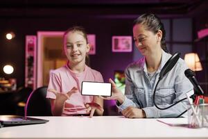 Daughter and mom being sponsored by partnering brand to do mockup mobile phone unboxing content. Small child and parent do influencer marketing, doing isolated screen smartphone product placement photo
