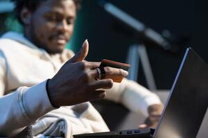 African american man adding payment method on website while in dimly lit apartment living room. Cheerful person excited to do online shopping, carefully typing credit card information, close up shot photo