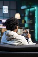 African american job candidate remotely being interviewed via internet videocall by manager. Man answering HR person interview questions during videoconference meeting while staying in apartment photo