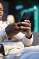 Focus on smartphone used by man in blurry background to compose messages, chatting with online friends. Close up shot of phone used by person to scroll on social media feed while at home photo