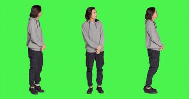 Young person looks at wristwatch standing against full body greenscreen backdrop, acting impatient on camera. Asian guy feeling stressed and irritated, waiting for a certain thing. photo