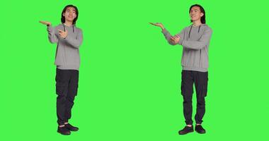 Asian person illustrating marketing ad over full body greenscreen, creating advertisement for new promotional slogan. Adult pointing at something on both sides of the studio, web commercial. photo
