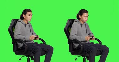 Person having fun with challenge over greenscreen backdrop, playing video games with joystick. Young asian man enjoying online gaming competition, video game player with skill. photo