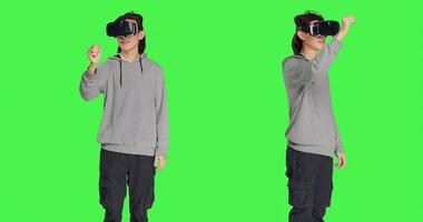 Male person using virtual reality gadget in studio with greenscreen backdrop, having fun with interactive 3d headset. Modern asian man enjoying artificial intelligence vr glasses. photo