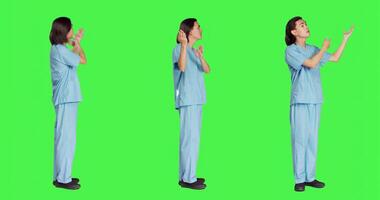 Asian medical assistant creates commercial for new medical ad campaign against greenscreen backdrop. Young nurse in uniform presents left or right sides, showing new advertisement slogan. photo