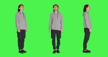 Asian natural adult appears proudly on camera, smiling over greenscreen full body background. Wearing comfortable clothing, young man seems to be cheerful and peaceful with confidence. photo