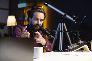 Content creator in home studio doing cool hand gesturing towards camera during live broadcast on online streaming platforms. Entertainer pointing fingers, captivating audience photo