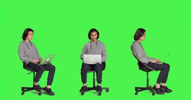 joven adulto hojeada el web en ordenador portátil en lleno cuerpo pantalla verde estudio, utilizando móvil computadora a navegar mediante páginas web en línea. persona sentado en silla y trabajando en inalámbrico ordenador personal, de moda chico. foto