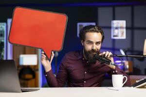 Influencer filming content, holding empty copy space sign, talking in professional microphone. Online star using cardboard bubble speech cutout to do influencer marketing, speaking in high tech mic photo