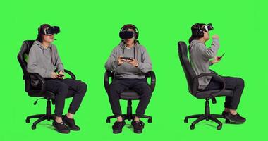 Adult uses vr gadgets for gameplay with smartphone app, sitting on gaming chair in isolated full body greenscreen. Asian male model playing multiplayer contest of virtual reality games. photo