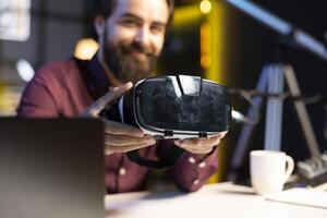 Close up shot of futuristic VR goggles held by tech specialist reviewing them for viewers. Internet star filming technology channel vlog for gadget enthusiasts, showcasing virtual reality headset photo