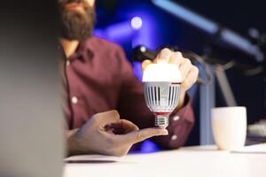 Close up shot of smart light bulb reviewed by tech enthusiast in studio discussing with audience about home improvement, telling viewers latest news in WiFi home automation industry photo