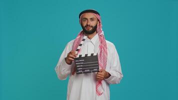 Middle eastern filmmaker holds clapboard used for scene takes on movie production, arab director using cinematography filming slate. Muslim person wearing traditional arab attire. photo