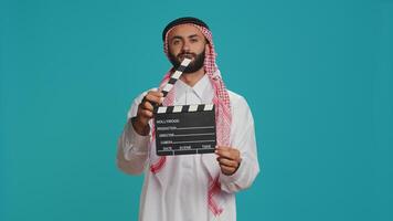 islámico adulto con claqueta usado para acción toma en película haciendo industria, joven cine productor utilizando rodaje producción pizarra. musulmán cineasta vistiendo tradicional atuendo y bufanda. foto