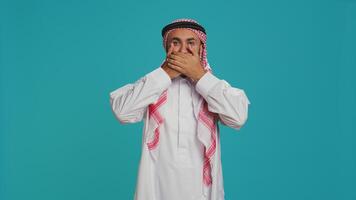 Male model covers eyes, ears and mouth on camera, presenting three wise monkeys symbol. Middle eastern person creating dont hear, see or speak metaphor sign, islamic clothing. photo