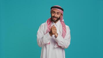 Hopeful arab man begging and pleading for something, holding hands in a prayer and showing belief. Middle eastern person being desperate and seeking help, having hope in blue studio. photo