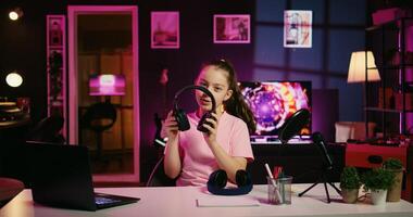 Kid influencer in studio using camera to review gaming keyboard, mouse and headphones. Child show host filming electronics haul, presenting wired computer peripherals to viewers photo