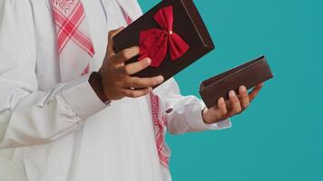 Islamic man opening giftbox with bow, receiving amazing present on his birthday. Middle eastern person feeling pleased about gift wrapped with ribbon, holiday package in studio. photo