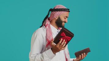 Arab person opening giftbox with ribbon, receiving beautiful present on his birthday. Middle eastern happy guy feeling excited about gift wrapped with box, holiday package. photo