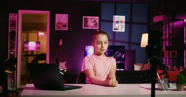 Zoom in shot of innocent little girl shooting video for social media platform in living room, talking about her day. Kid entertaining fans, doing content creation using professional recording tech photo