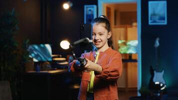 Energetic child dancing and singing, using phone attached to selfie stick to shoot video for social media platforms in living room. Kid entertaining followers, filming with smartphone photo