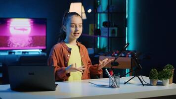 Energetic child shooting video for social media platform in living room, talking about her day. Cute kid entertaining followers, doing content creation in neon lit apartment photo