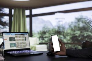 Influential CEO holding phone with white screen layout, working from his luxurious alpine resort. Wealthy entrepreneur examining financial resources and blank display on smartphone app. photo