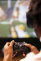 Close up shot of controller held by gamer sitting in front of gigantic television set displaying console game. Joystick used by homeowner enjoying gaming session on smart TV, relaxing in living room photo