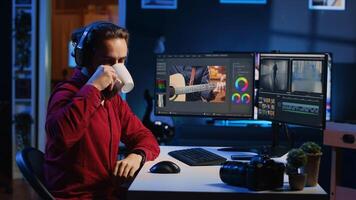 Videographer using editing software to assemble footage into cohesive final result while enjoying cup of coffee. Specialist color correcting clips while listening music in headphones photo