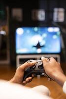 Focus shot on man holding controller in apartment, playing videogames on smart TV display in blurry background. Gamer on sofa using joypad to participate in game on console attached to television set photo