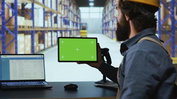 Packaging engineer looking at tablet with greenscreen in depot, working in warehouse with blank copyspace template. Professional depot employee examines device with isolated display. photo