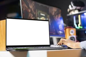 Focus on isolated screen laptop on desk next to player playing singleplayer videogame in neon lit apartment. Close up shot of mockup notebook and man enjoying game on computer photo