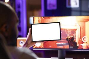 Player looking at isolated screen tablet, taking break from playing singleplayer videogame on gaming computer, close up. Man in home using mockup portable device while enjoying game photo