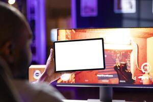 Player looking at isolated screen tablet, taking break from playing singleplayer videogame on gaming computer, close up. Man in home using mockup portable device while enjoying game photo