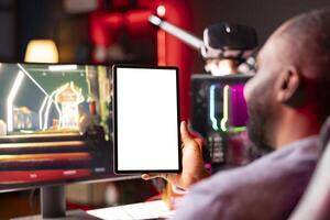 Isolated screen tablet held by gamer competing in online multiplayer videogame at home. Mockup portable device utilized by man playing on gaming PC in neon illuminated apartment photo