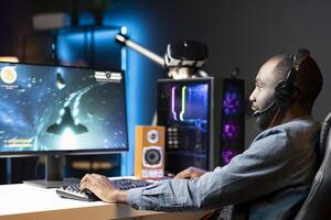 Gamer plays online multiplayer spaceship videogame with friends, relaxing. Player talking with teammates, flying spacecraft, enjoying leisure time in neon lights adorn living room photo