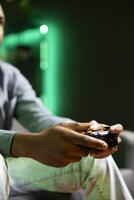 Gamer on couch using controller and headphones to play videogame in neon lit apartment, close up. Player in RGB illuminated living room using high tech gaming console joystick photo